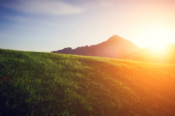 Gramado verde com uma montanha ao pôr do sol — Fotografia de Stock