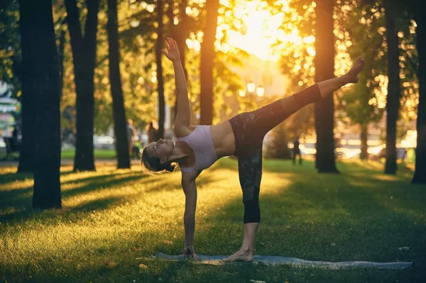 Belle jeune femme pratique le yoga asana Ardha Chandrasana - Demi-lune pose dans le parc au coucher du soleil — Photo