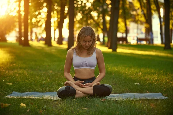 Belle jeune femme pratique le yoga asana Padmasana - Lotus pose dans le parc au coucher du soleil — Photo