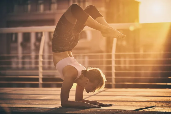 Mladá žena cvičí jógu, stojící v Vrischikasana Scorpion pozice na terase při západu slunce — Stock fotografie