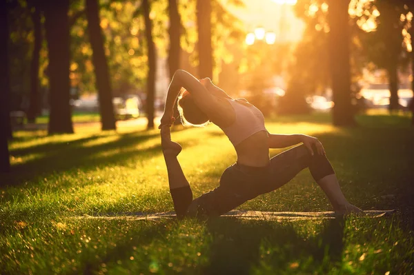 Krásná mladá žena praktiky yogové ásány král Holub pozice rajakapotasana v parku při západu slunce — Stock fotografie