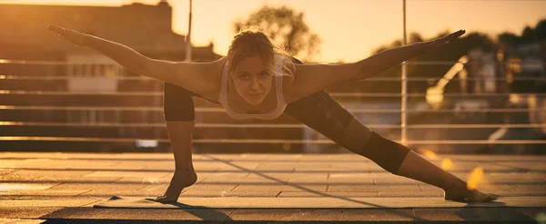 Beautiful young woman practices yoga in the terrace at sunset — Stock Photo, Image