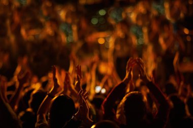 Bir müzik festivalinde seyirciler ellerini kaldırdı ve sahnenin üstünden ışıklar süzülüyor..