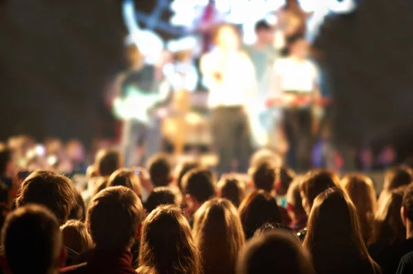 Audience with hands raised at a music festival and lights streaming down from above the stage. — Stock Photo, Image