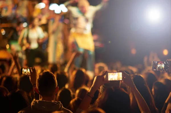 Közönség felemelt kézzel egy zenei fesztiválon, és a színpadról sugárzó fények.. — Stock Fotó