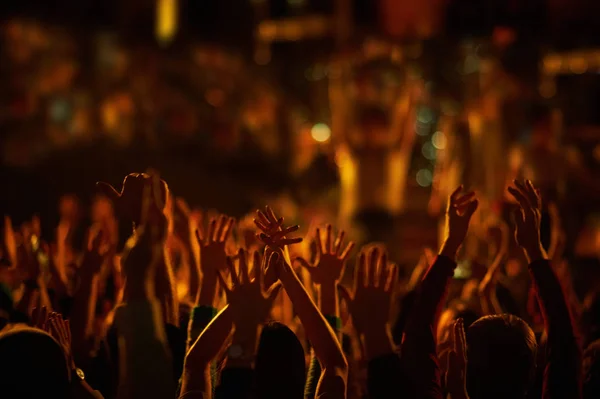 Közönség felemelt kézzel egy zenei fesztiválon, és a színpadról sugárzó fények.. — Stock Fotó