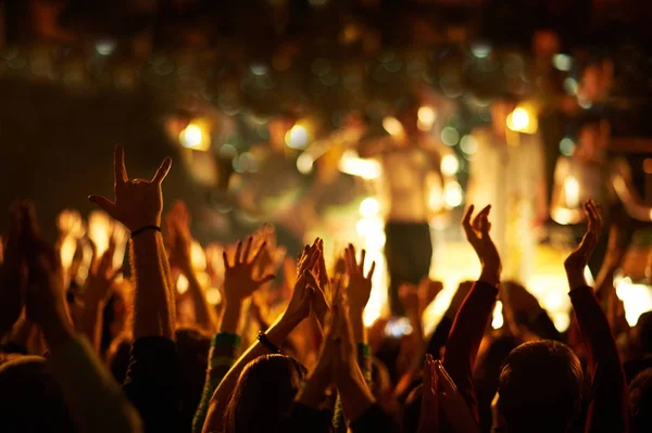 Publiek met opgeheven handen op een muziekfestival en lichten die van boven het podium naar beneden stromen. — Stockfoto