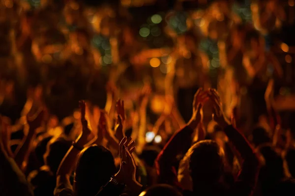 Audience with hands raised at a music festival and lights streaming down from above the stage. — Stock Photo, Image