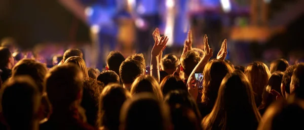 Зрители с поднятыми руками на музыкальном фестивале и огнями, струящимися сверху сцены. Стоковое Фото