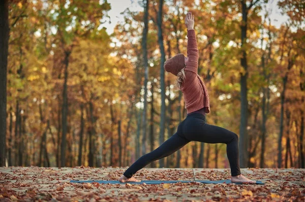 Красивая молодая женщина практикует йогу asana Virabhadrasana 1 - воин поза на деревянной палубе в осеннем парке . — стоковое фото