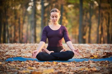 Yoga asana Padmasana - Lotus poz sonbahar Park ahşap güverte üzerinde güzel genç kadın meditasyon.