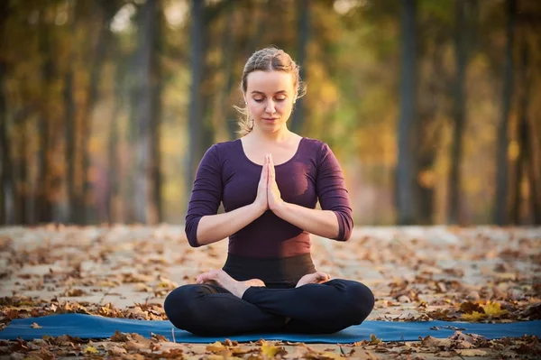 Mulher bonita medita em ioga asana Padmasana - pose de lótus no convés de madeira no parque de outono . — Fotografia de Stock