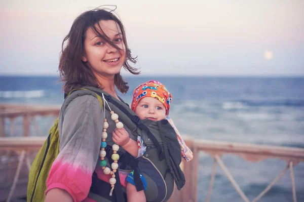 Молода мама на пляжі зі своєю дитиною в слінгу — стокове фото