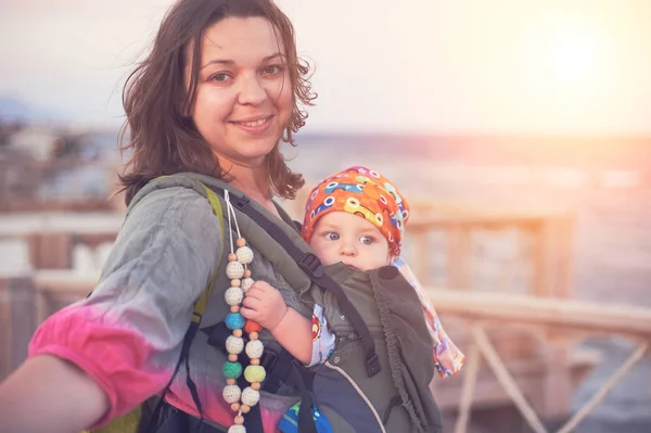 Молода мама на пляжі зі своєю дитиною в слінгу — стокове фото