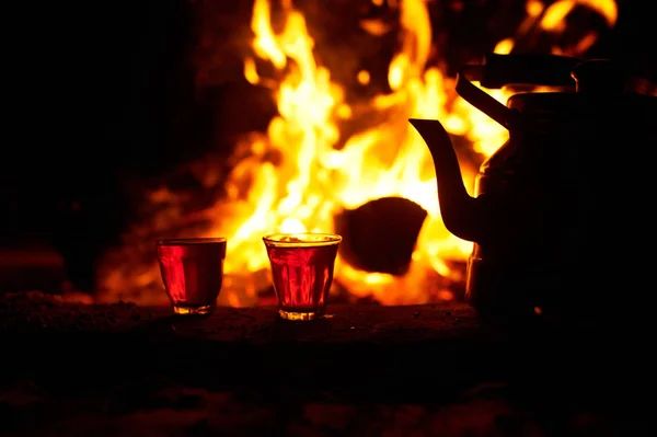 Copos com chá perto do fogo com madeira flamejante à noite — Fotografia de Stock