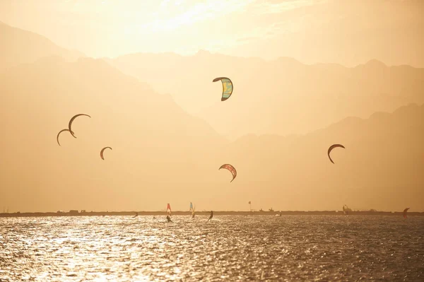 Sportmans kitesurf sulla superficie del mare contro le montagne al tramonto — Foto Stock