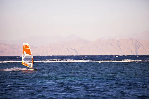 Sportman windsurfer στην επιφάνεια της θαλάσσης εναντίον βουνά κατά το ηλιοβασίλεμα — Φωτογραφία Αρχείου