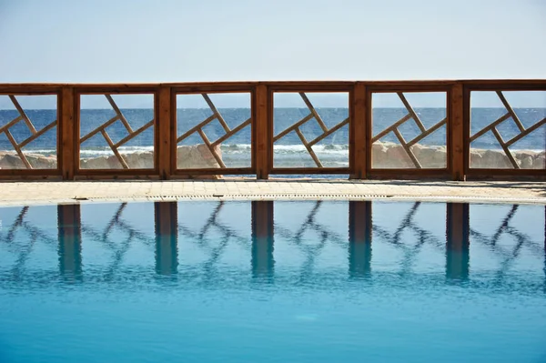 Fence of the resort pool reflected on the water. Pure blue sky on the background.