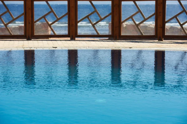 Fence of the resort pool reflected on the water. Pure blue sky on the background.