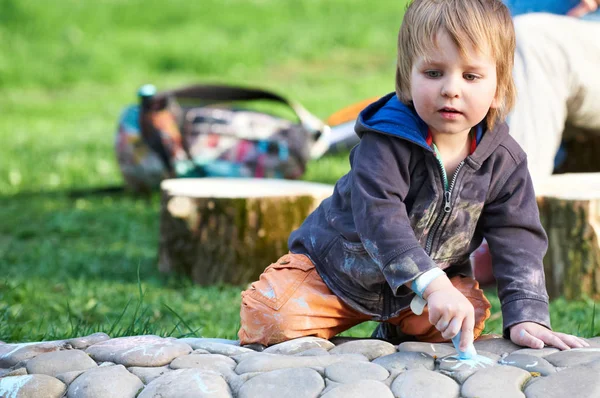 Kleiner Junge zeichnet mit Gehwegkreide im Park. — Stockfoto