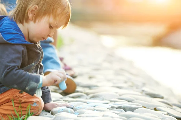 Jongetje tekenen met stoep krijt in het park. — Stockfoto