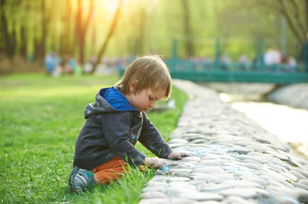 Kleiner Junge zeichnet mit Gehwegkreide im Park. — Stockfoto