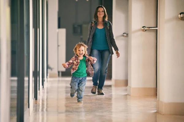 Маленький хлопчик біжить в торговому центрі зі своєю мамою на фоні . — стокове фото