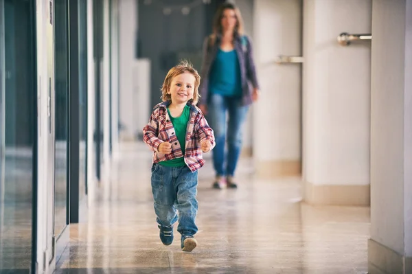 Kleiner Junge läuft im Einkaufszentrum mit seiner Mutter im Hintergrund. — Stockfoto