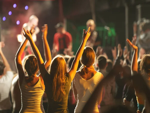 Audience with hands raised at a music festival and lights streaming down from above the stage. — Stock Photo, Image