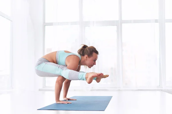 Beautiful woman practices handstand yoga asana Tittibhasana - firefly pose at the yoga studio