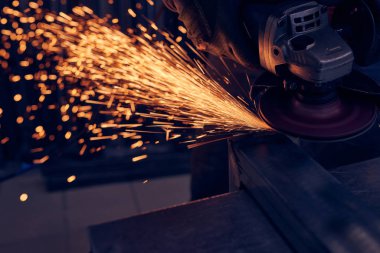 Öğütücüyle metal kesen bir işçi. Demir öğütürken kıvılcımlar