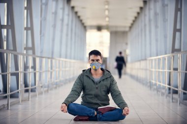 Bir adam boş halka açık bir yerde maske takarak meditasyon yapıyor. Coronavirus konsept fotoğrafı