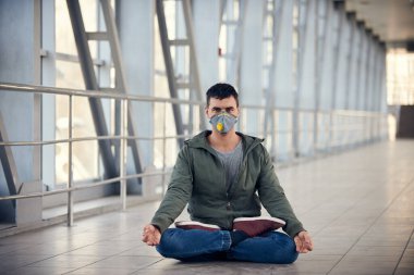 Bir adam boş halka açık bir yerde maske takarak meditasyon yapıyor. Coronavirus konsept fotoğrafı