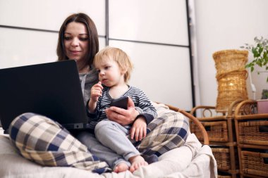 Annem evde dizüstü bilgisayarla çalışıyor ve bebeğiyle oynuyor. Karantina konsepti.