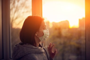 Gün batımında pencerenin yanında bir kadın virüs salgını için izolasyonda. Evde kal konsepti.