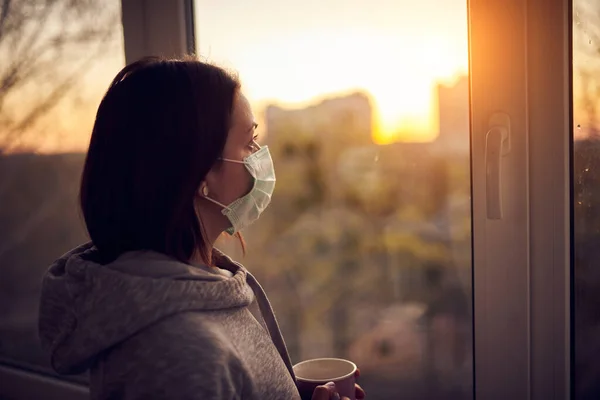 Woman near window at sunset in isolation at home for virus outbreak. Stay home concept.