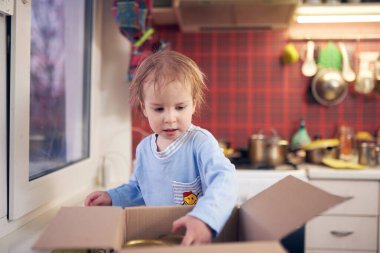 Şirin bir çocuk, karantina sırasında evdeki mutfaktaki bir kutudan metal kutular çıkarıyor..