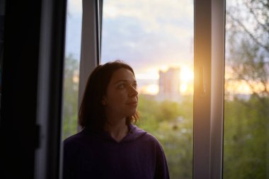 Gün batımında pencerenin yanında bir kadın virüs salgını için izolasyonda. Salgın konseptinin sonu.