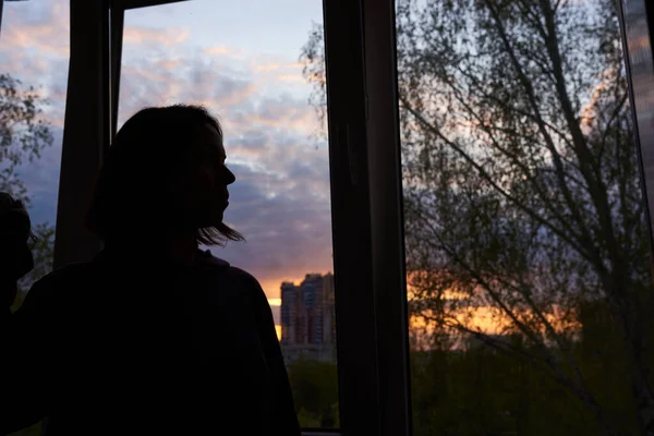 Woman near window at sunset in isolation at home for virus outbreak. End of epidemic concept.