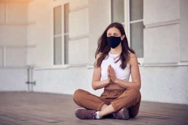 Kadın boş halka açık bir yerde maske takarak meditasyon yapıyor. Coronavirus salgını konsept fotoğrafı.