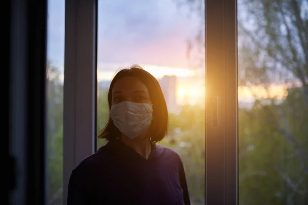 Woman near window at sunset in isolation at home for virus outbreak. Stay home concept.