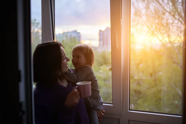 Moeder Met Baby Kijkt Uit Het Raam Bij Zonsondergang Isolatie — Stockfoto