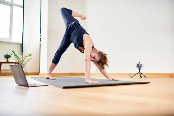 Woman doing yoga online. Computer and camera in her living room. Healthy lifestyle and distance work concepts.