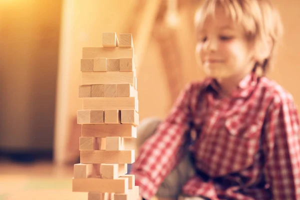 Preschool cute boy playing in a table game with wooden blocks at home. Players take turns removing one block at a time from a tower. Each block removed is then placed on top of the tower.
