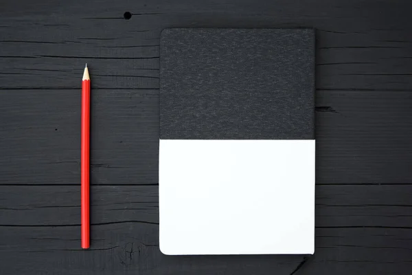 Blank notebook and pencil. Red pencil and blank black and white notebook on black wooden desk