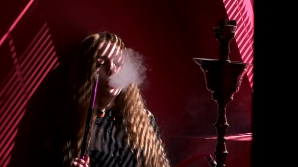 Menina fuma uma shisha na janela uma luz traseira endireita seu cabelo — Vídeo de Stock