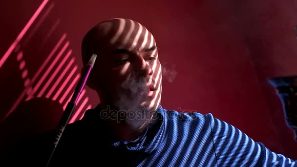 Bald man smoking a shisha hookah at the window light through the blinds — Stock Video