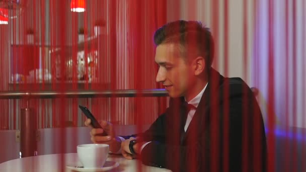Jonge man glimlacht en maakt gebruik van de smartphone in een restaurant — Stockvideo