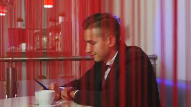 Takım elbiseli genç adam gülümsüyor ve smartphone bir restoranda kullanır