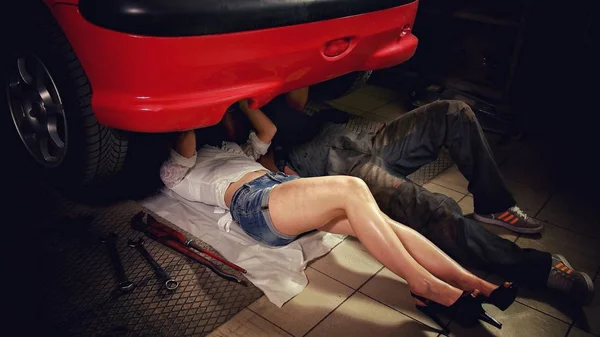 Hombre y una mujer yacen debajo del coche en el taller y reparar el coche Imágenes de stock libres de derechos